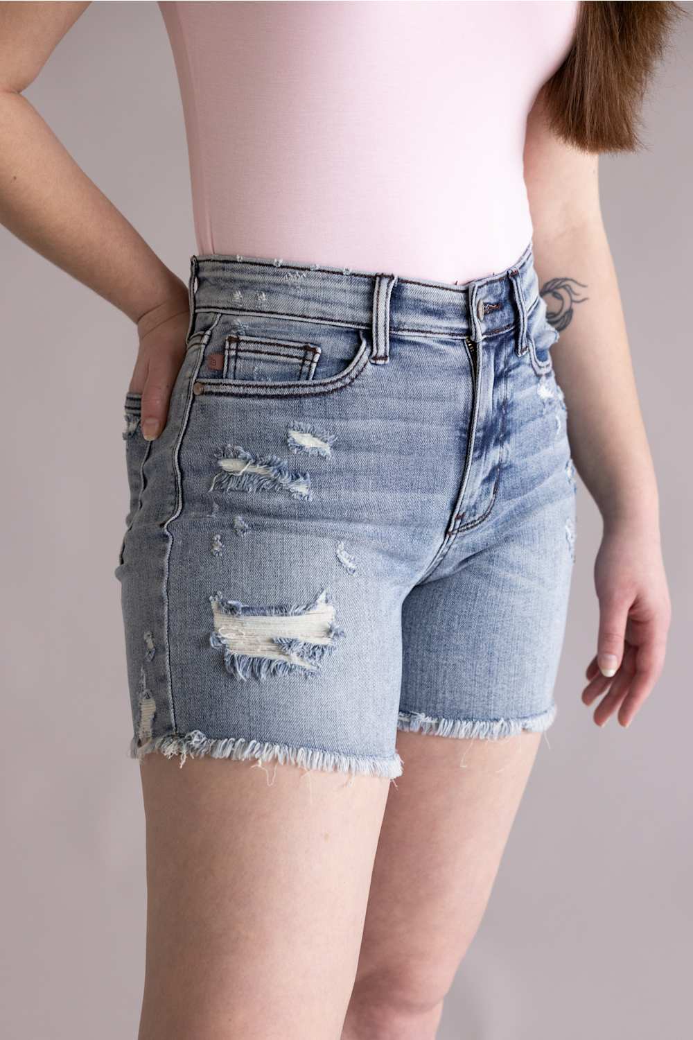 Judy Blue High Rise Distressed Fray Hem Denim Shorts for Women; Denim shorts with distressed details on a neutral background