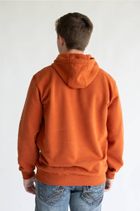Man wearing a burnt orange colored hoodie, with Carhartt logo down the left arm sleeve. 