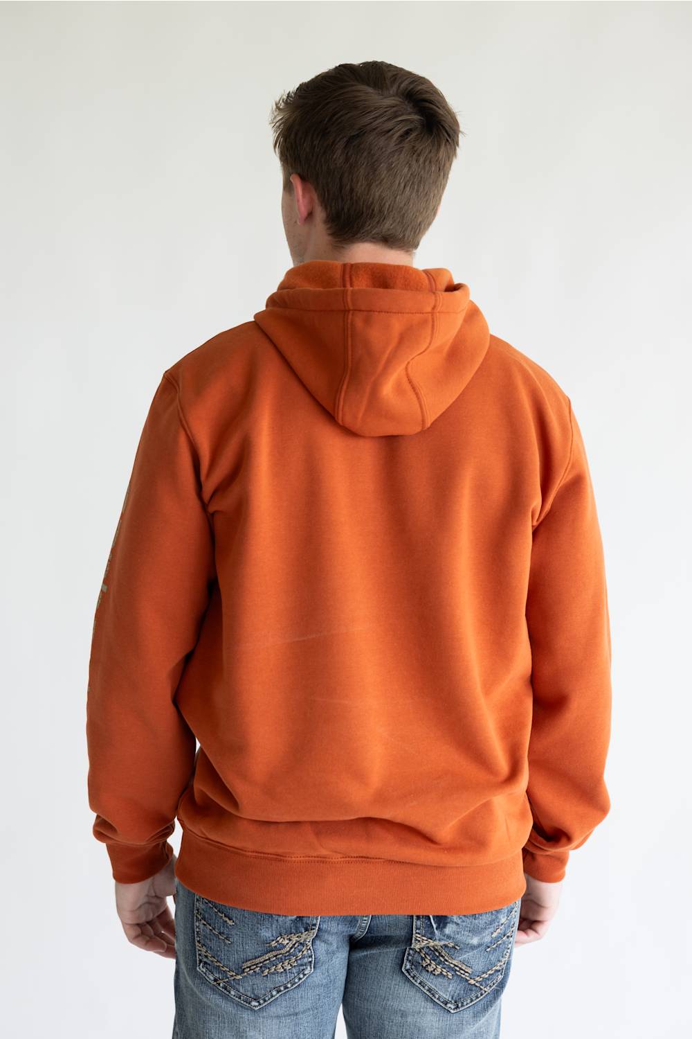 Man wearing a burnt orange colored hoodie, with Carhartt logo down the left arm sleeve. 