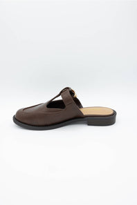 A dark brown leather mule sandal with a T-strap and a small gold-tone buckle detail, shown from a side profile on a light gray background.