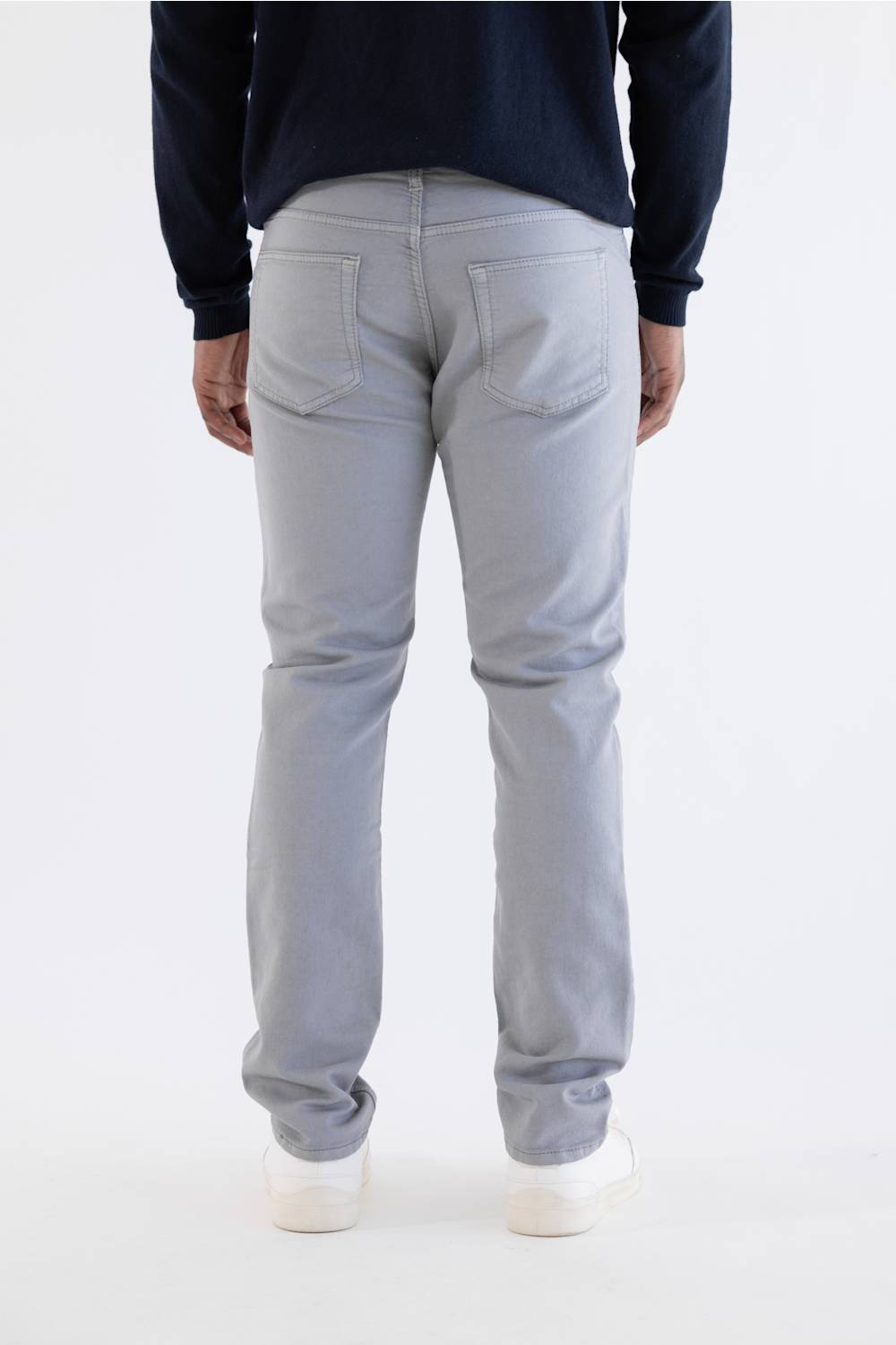 A person shown from the back wearing light gray slim-fit jeans, a dark navy long-sleeve top, and white sneakers against a plain white studio background.