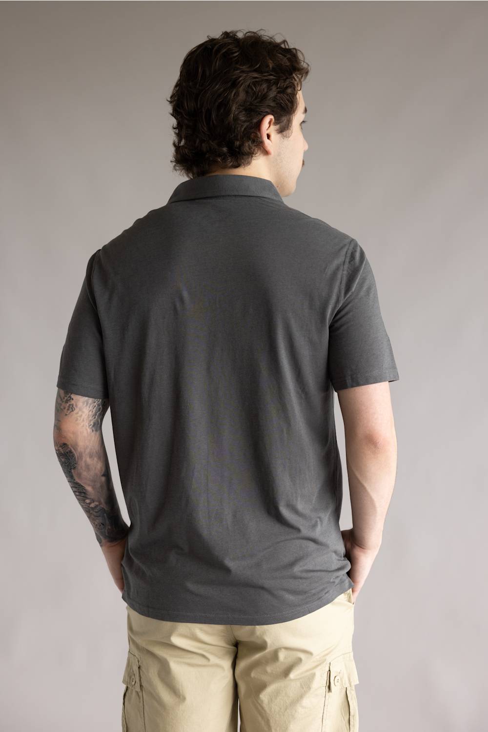 Kuhl De Facto Polo Shirt for Men in Carbon; Man wearing a dark gray polo shirt and beige pants against a plain background