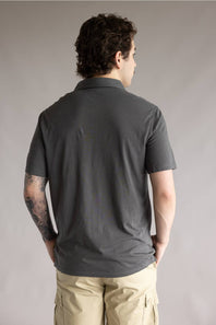 Kuhl De Facto Polo Shirt for Men in Carbon; Man wearing a dark gray polo shirt and beige pants against a plain background