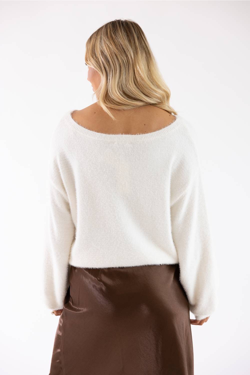 A woman shown from the back wearing a fuzzy off-white cropped sweater and a brown skirt, photographed against a plain white studio background.