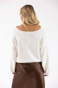 A woman shown from the back wearing a fuzzy off-white cropped sweater and a brown skirt, photographed against a plain white studio background.