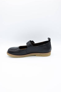 A black slip-on shoe with a tan gum sole, shown from a side profile view against a plain white background.