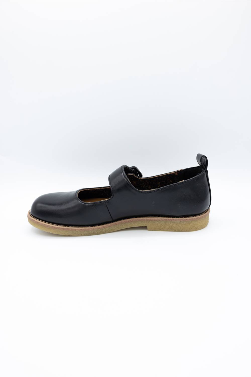 A black slip-on shoe with a tan gum sole, shown from a side profile view against a plain white background.