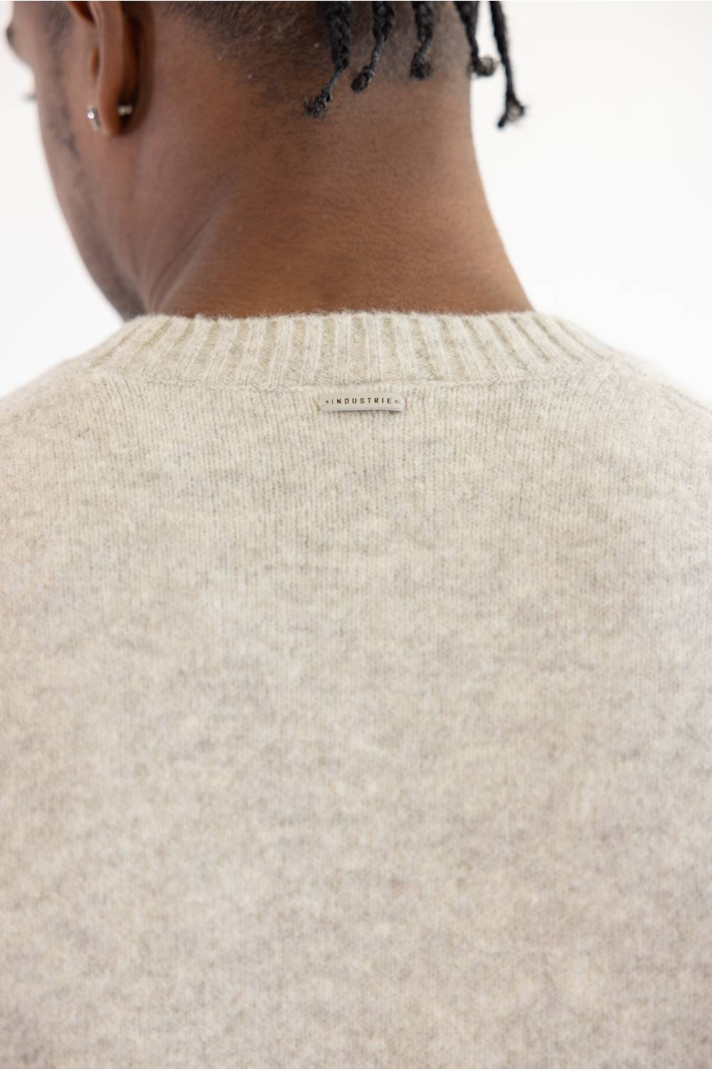Close-up back view of a person wearing a cream-colored knit sweater, showing the ribbed crew neck and a small woven label at the center.