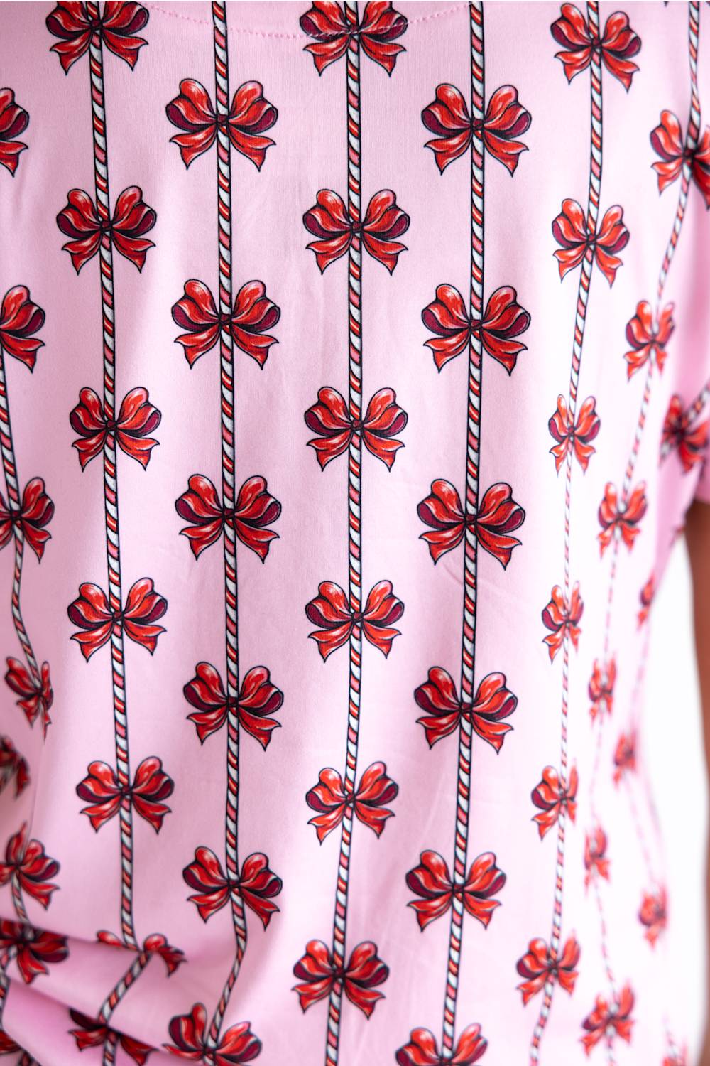 A close-up of a light pink garment featuring a repeating pattern of red gift bows and vertical striped ribbons.