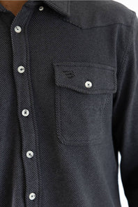 Close-up of a dark charcoal gray textured button-down shirt with a chest pocket and silver buttons.