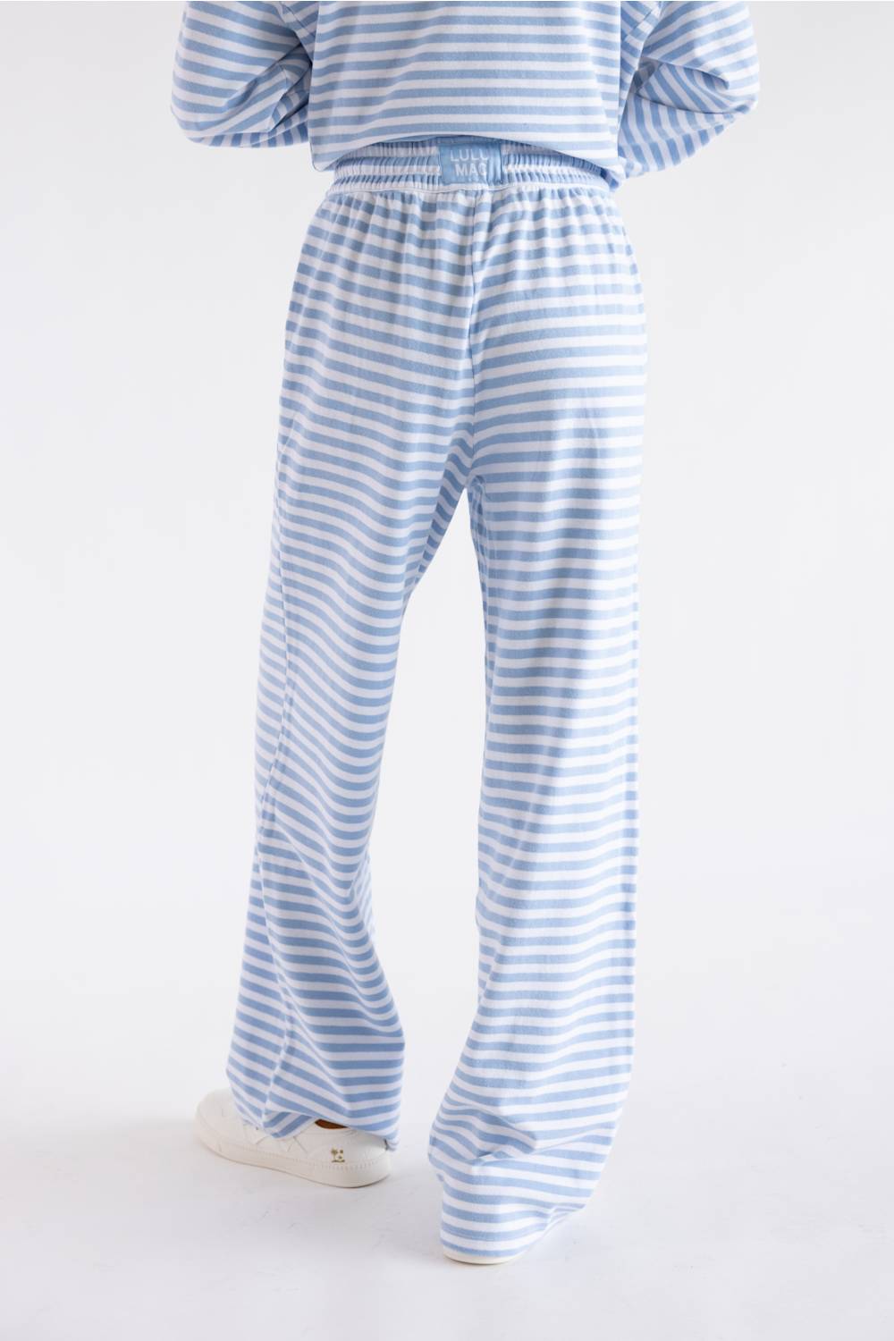 A person shown from the back wearing light blue and white striped lounge pants and a matching striped top, standing against a plain white studio background.