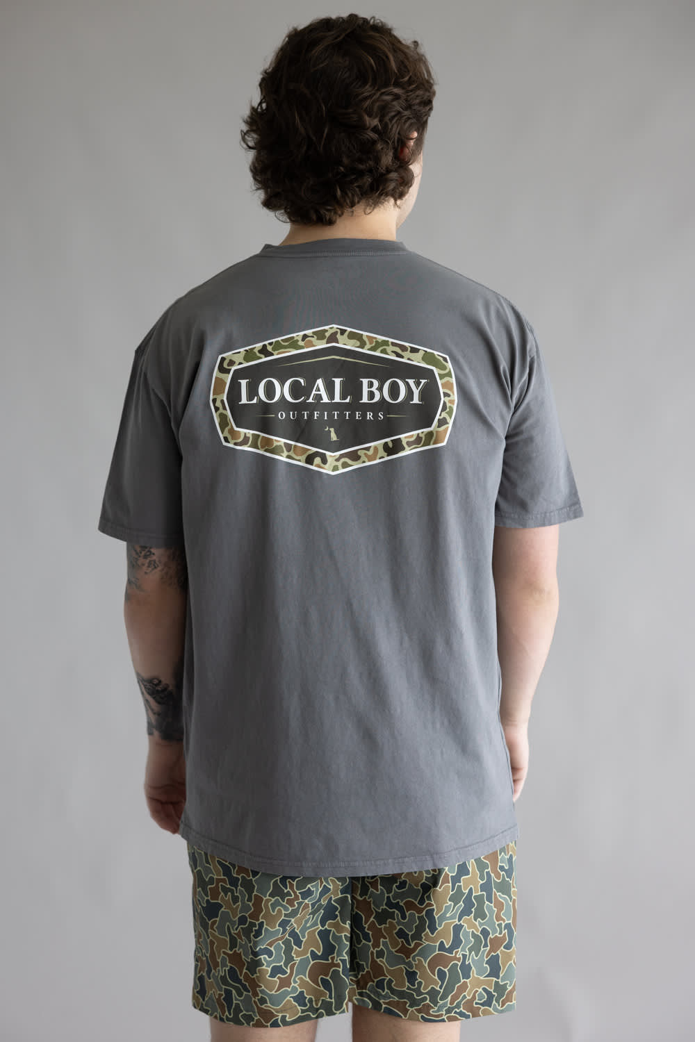 Local Boy Vintage Emblem T-Shirt for Men in Grey; Person wearing a gray t-shirt with 'Local Boy Outfitters' logo on the back, standing against a plain background.