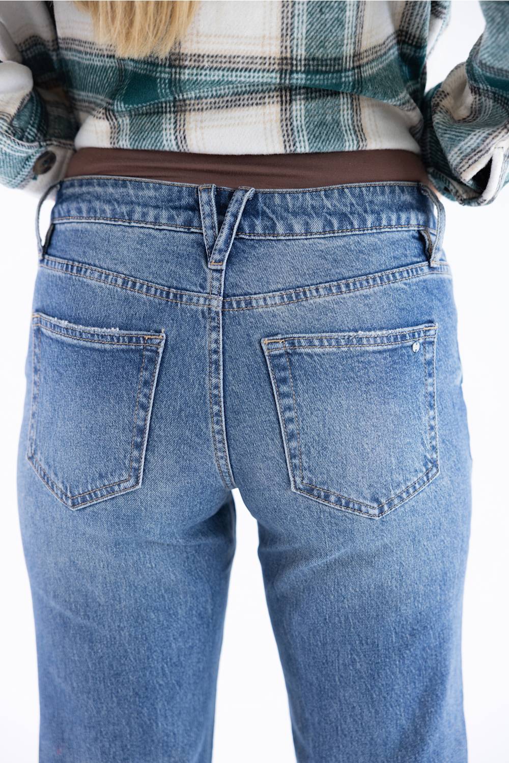 Rear view of a person wearing light blue denim jeans and a green and white plaid shirt against a plain white background.