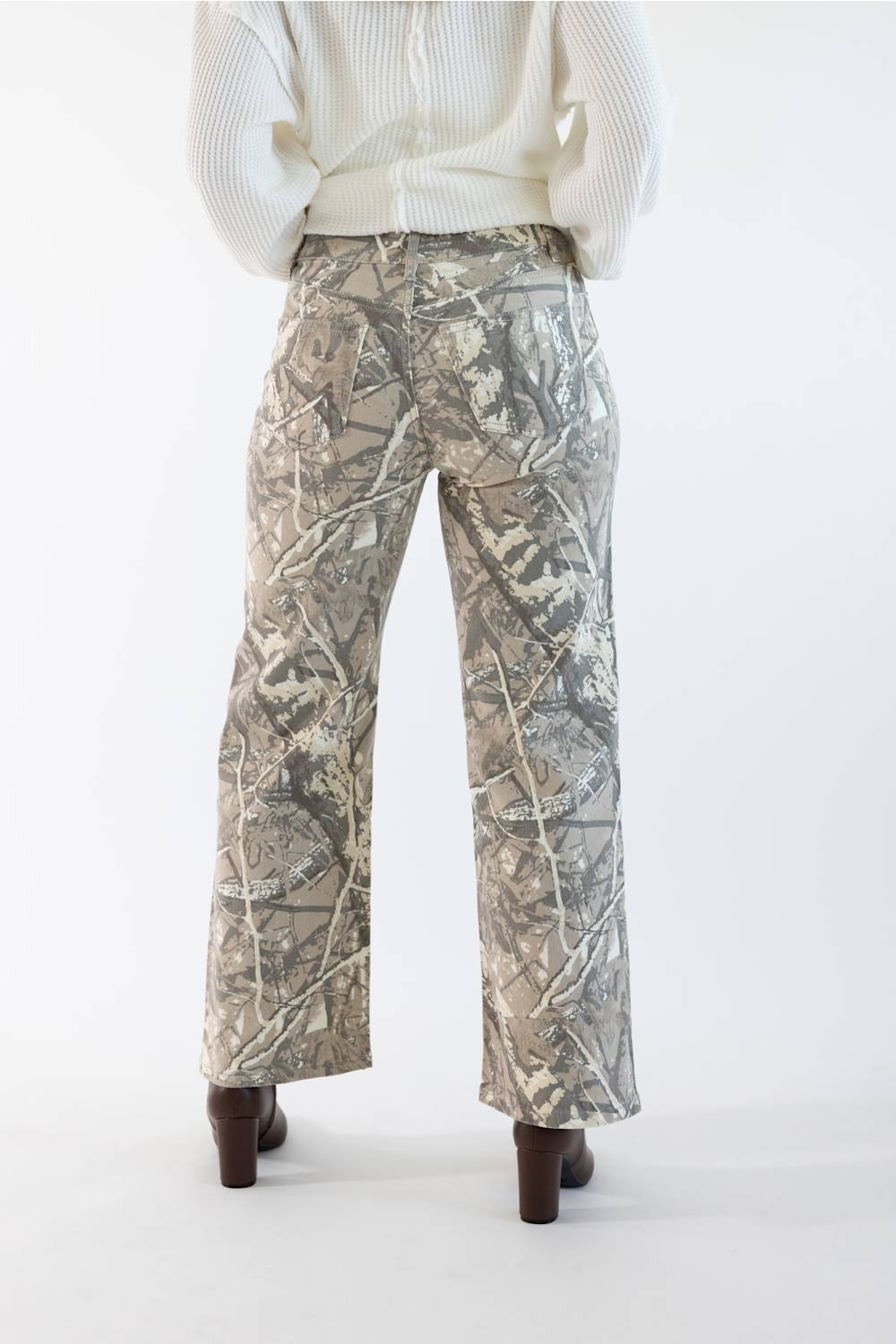 A person shown from the back wearing camouflage pants with a cream ribbed cardigan and dark brown heels, photographed against a plain white studio background.