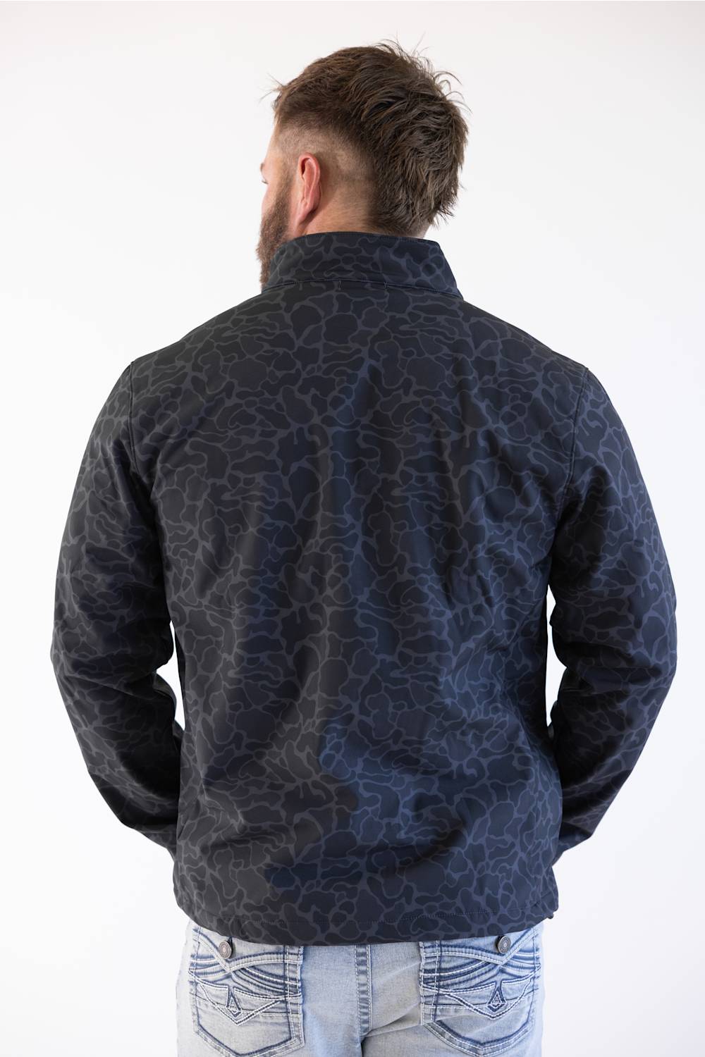 A man viewed from behind wearing a dark navy blue patterned jacket and light blue jeans against a plain white background.