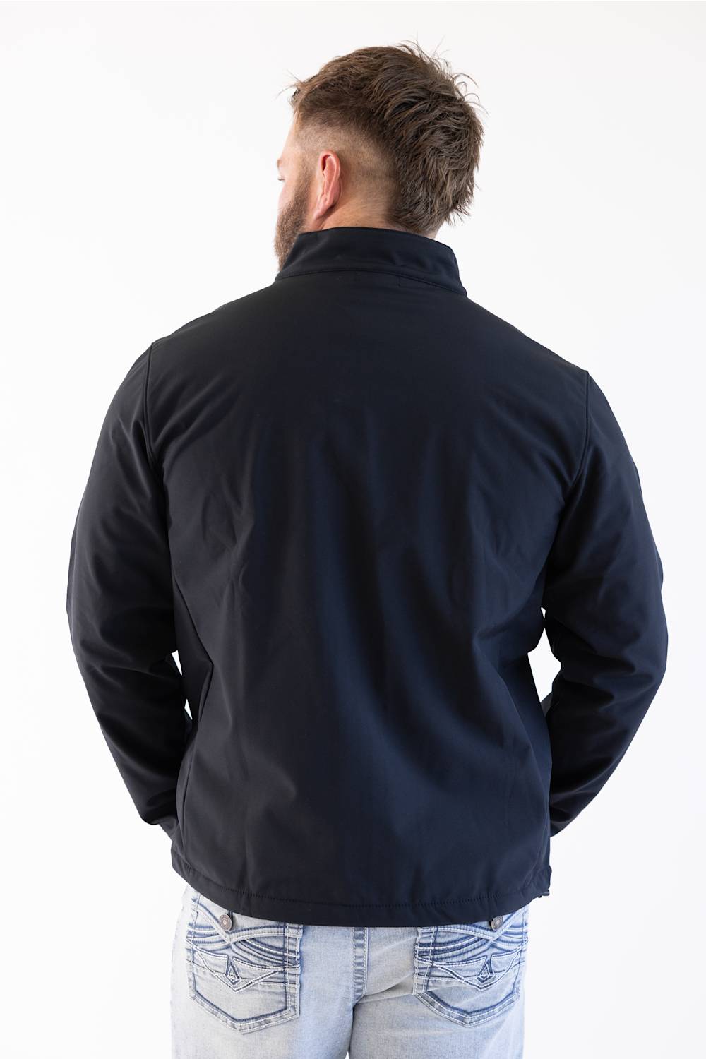 A man viewed from behind wearing a dark navy blue jacket and light blue jeans against a plain white background.
