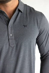 A close-up of a man wearing a dark gray long-sleeve polo shirt with a small black embroidered dog logo on the left chest.