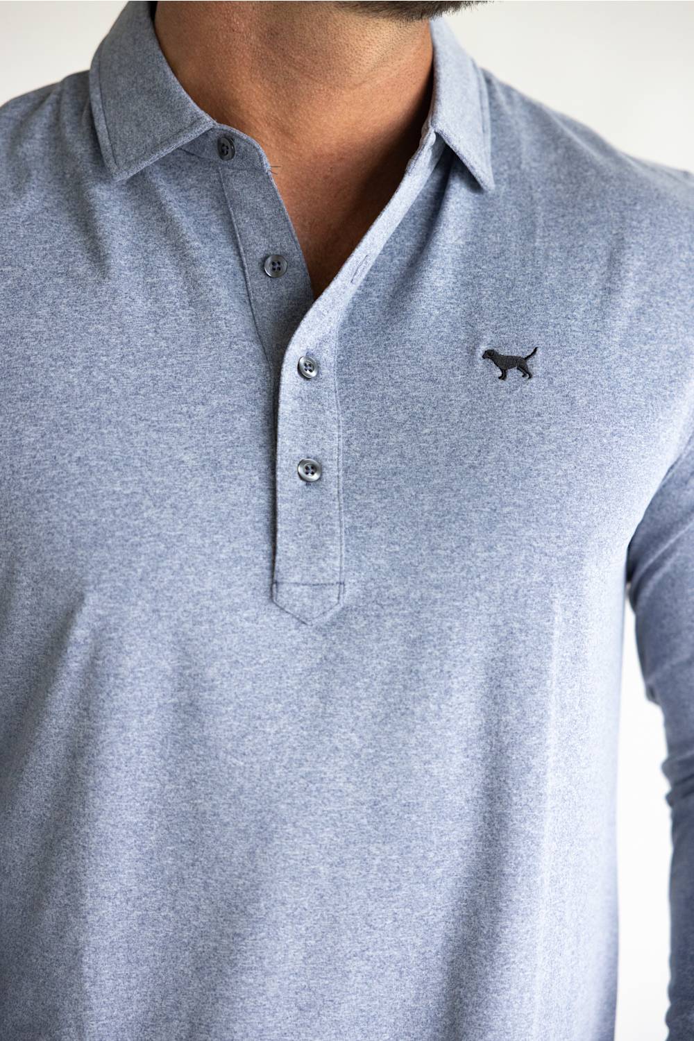 A close-up of a man wearing a light heather gray long-sleeve polo shirt with a three-button placket and a small black embroidered dog logo on the left chest.