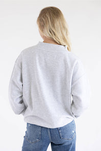 A woman viewed from behind wearing a light gray heather crewneck sweatshirt and blue jeans against a plain white background.