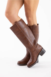 A pair of knee-high brown leather boots with a low block heel, shown on a model's legs against a plain white background.