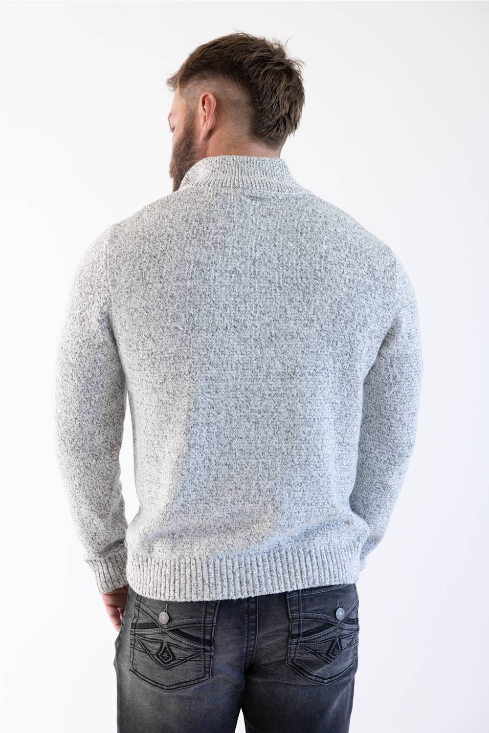 A man viewed from behind wearing a light gray marled knit sweater and dark gray jeans against a plain white background.