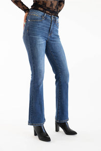 A person wearing medium-wash blue denim jeans with a slight flare at the hem, paired with black pointed-toe heeled boots against a plain white studio background.