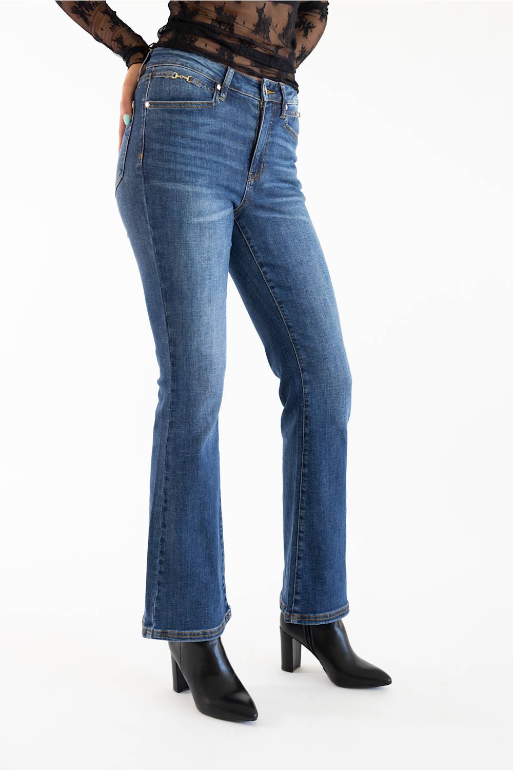 A person wearing medium-wash blue denim jeans with a slight flare at the hem, paired with black pointed-toe heeled boots against a plain white studio background.