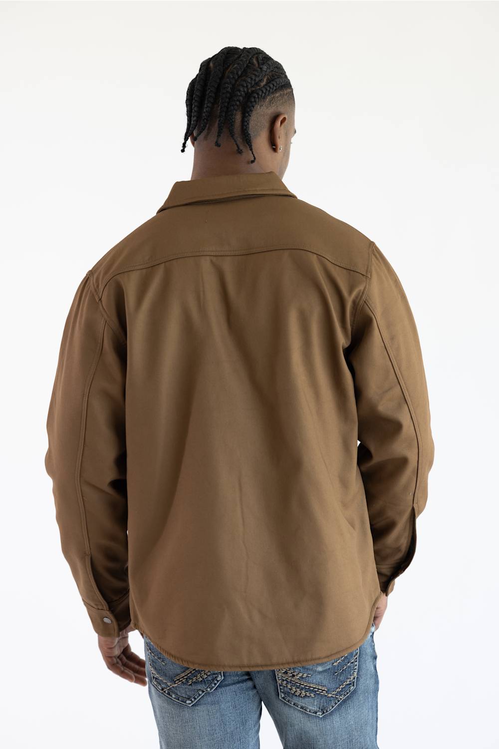 A man viewed from behind wearing a brown long-sleeve overshirt and blue jeans against a plain white background.