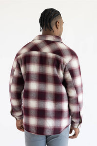 A man viewed from the back wearing a long-sleeve plaid flannel shirt in burgundy, cream, and gray, paired with light gray pants, against a plain white background.
