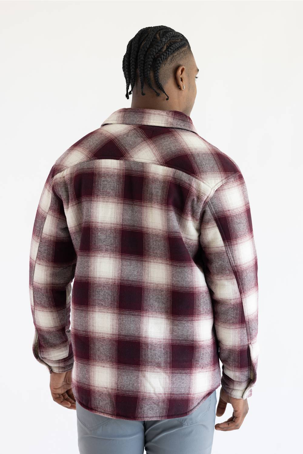 A man viewed from the back wearing a long-sleeve plaid flannel shirt in burgundy, cream, and gray, paired with light gray pants, against a plain white background.