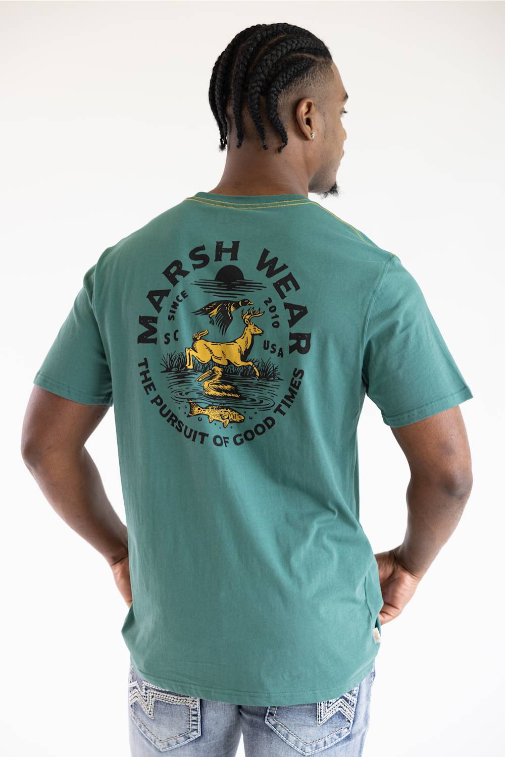 A man wearing a teal green t-shirt with a large back graphic that reads 'MARSH WEAR' and features a yellow deer and black text, shown from behind against a white background.