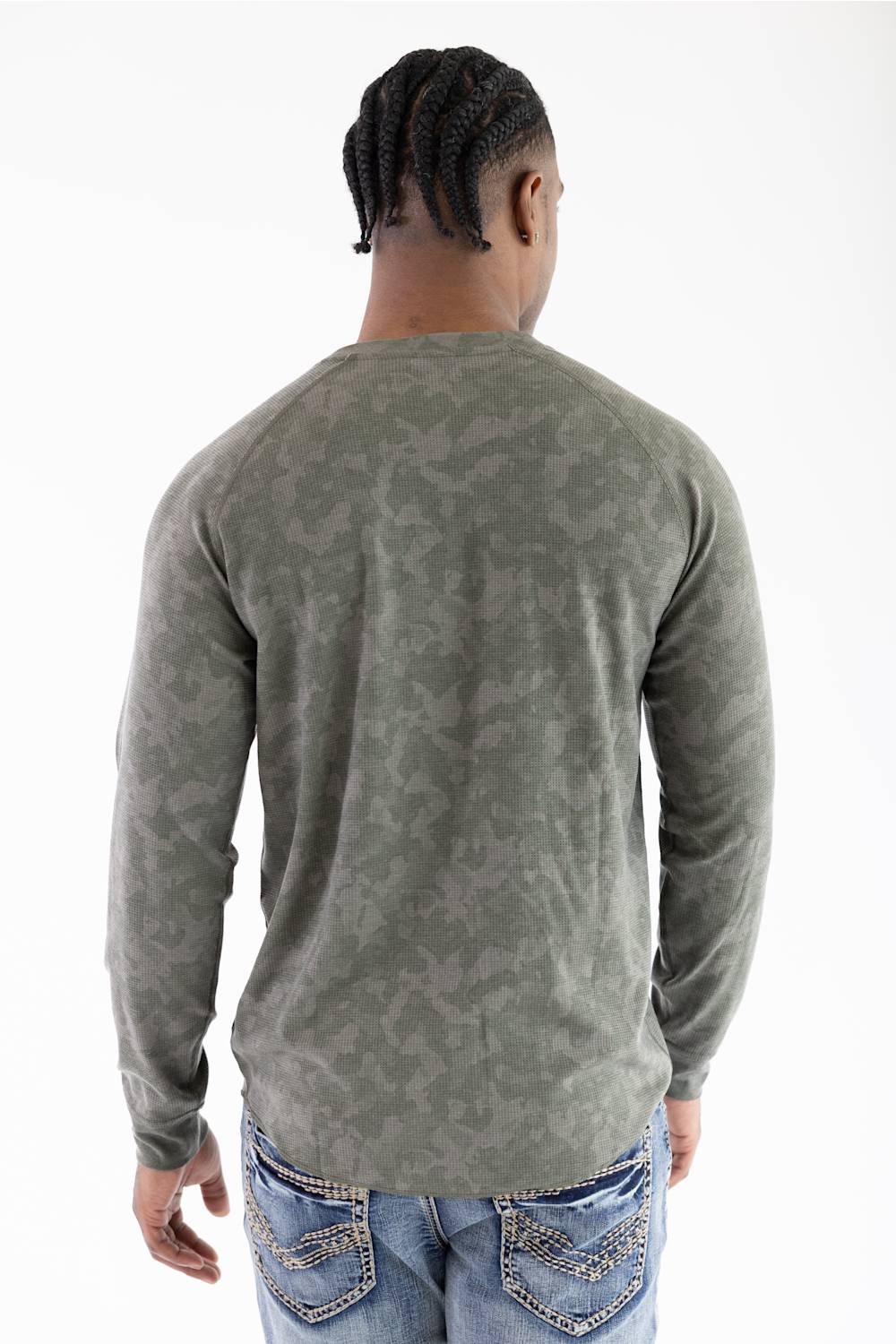 Back view of a model wearing the Marsh Wear Surfside Waffle Knit Shirt in Fossil Foxhole Camo green, showcasing the long-sleeve waffle-textured fabric and raglan shoulder seam detailing, paired with light-wash blue jeans featuring decorative back pocket stitching
