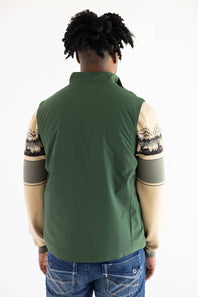 A person shown from the back wearing an olive green sleeveless vest layered over a beige and gray patterned long-sleeve shirt, paired with blue jeans, against a plain white background.