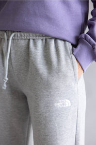 Close-up of a person wearing heather gray sweatpants with a white embroidered The North Face logo on the left thigh, paired with a lavender sweatshirt.