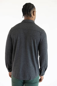 A man viewed from behind wearing a dark heather gray long-sleeve button-up shirt and green pants, standing against a plain white background.