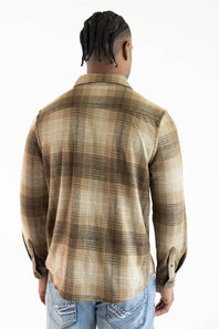 A man viewed from behind wearing a brown and beige plaid button-down shirt and blue jeans against a plain white background.