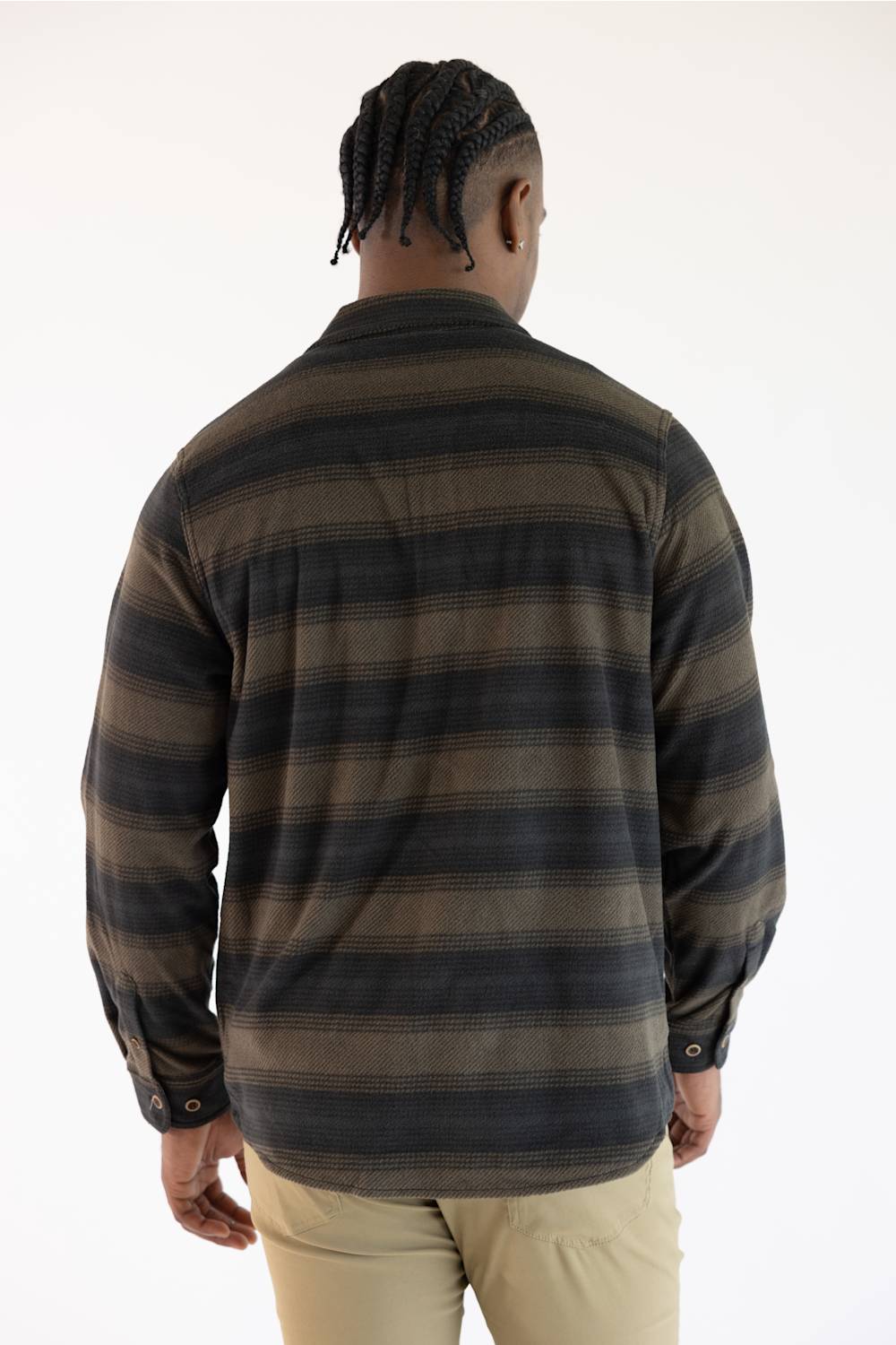 A man viewed from behind wearing a long-sleeve striped flannel shirt in dark brown and black, paired with khaki pants, against a plain white background.