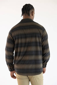 A man viewed from behind wearing a long-sleeve striped flannel shirt in dark brown and black, paired with khaki pants, against a plain white background.