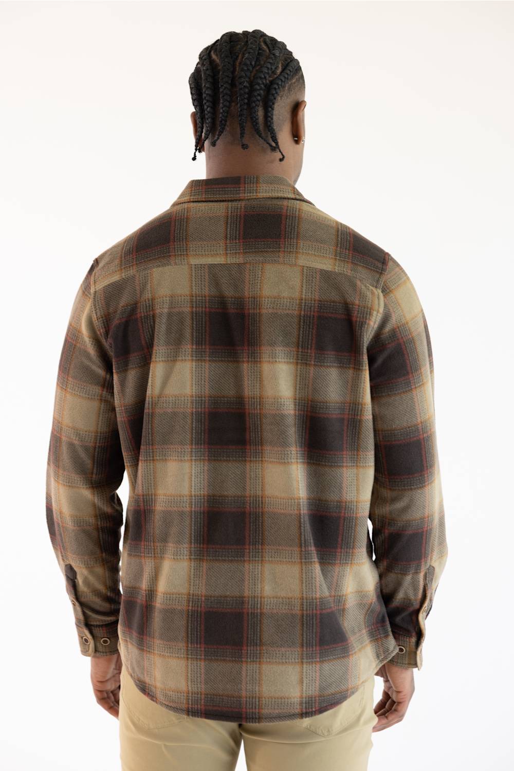 A man viewed from behind wearing a long-sleeve plaid flannel shirt in brown, beige, and black, paired with khaki pants, against a plain white background.