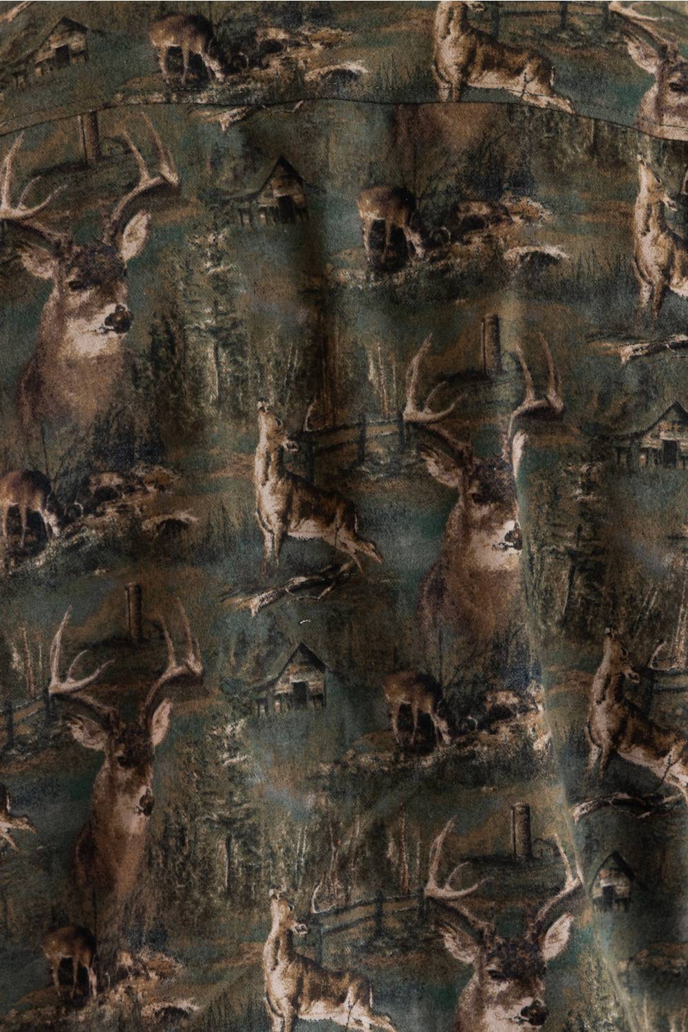 A close-up of a camouflage-patterned fabric featuring a woodland print with deer, trees, and small cabins in muted green, brown, and gray tones.