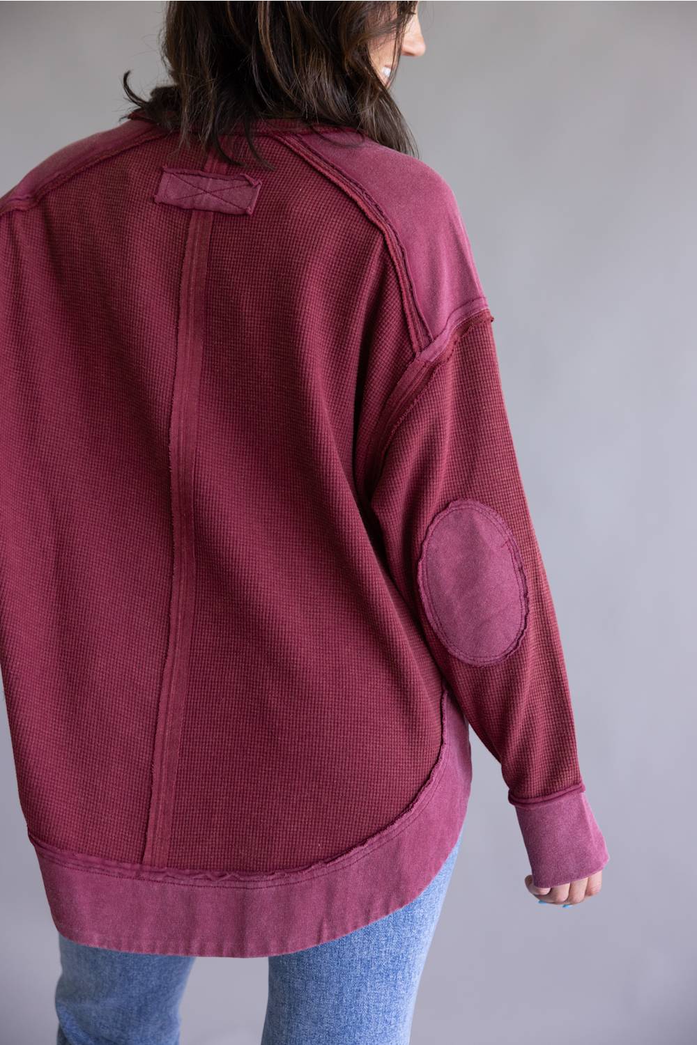 Woman wearing a burgundy sweatshirt with elbow patches on a plain background