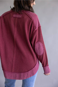 Woman wearing a burgundy sweatshirt with elbow patches on a plain background