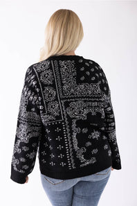 A woman viewed from behind wearing a black knit sweater with a white bandana print pattern, paired with blue jeans, against a plain white background.