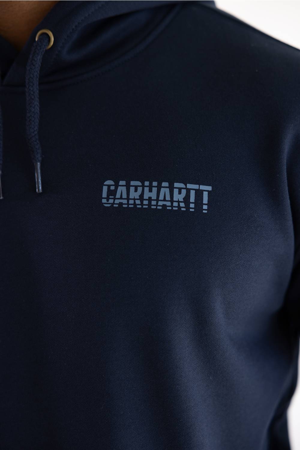 Close-up of a navy blue hooded sweatshirt with the Carhartt logo printed in a matching dark blue on the chest, featuring a drawstring hood and gold-toned ring detail.