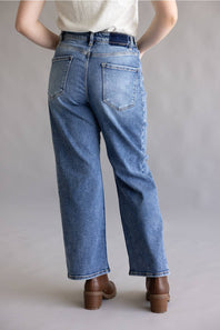 Close-up of a person's hands adjusting the waistband and button of blue denim jeans, wearing a light gray heathered t-shirt.