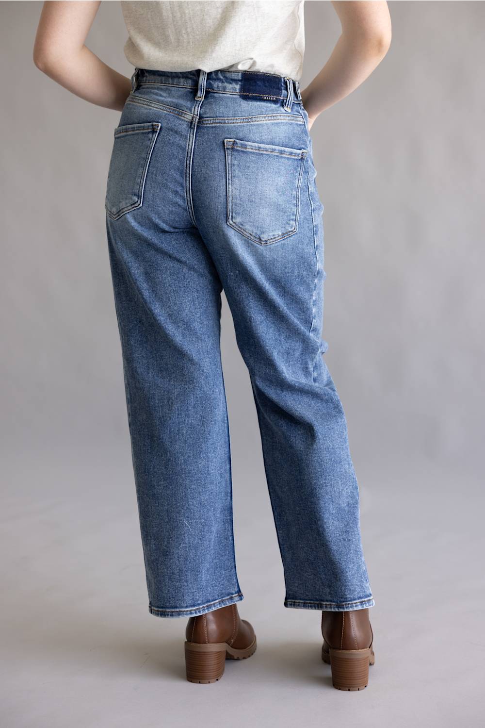 Close-up of a person's hands adjusting the waistband and button of blue denim jeans, wearing a light gray heathered t-shirt.