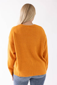 A woman viewed from behind wearing a bright orange knit sweater and blue jeans against a plain white background.