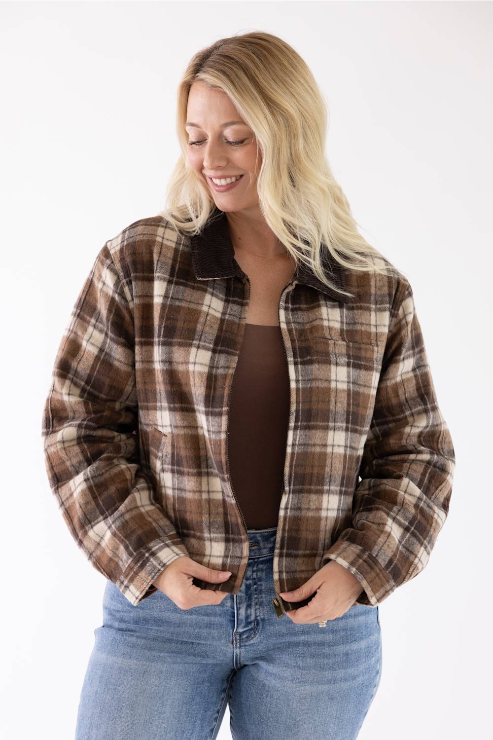 Detail shot of the Brown/Cream Plaid Barn Jacket showing the front open, with the model zipping the jacket over a brown top, highlighting the texture and contrasting collar against light jeans.