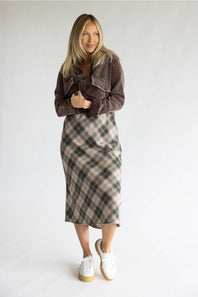A woman modeling a brown corduroy jacket and a brown, beige, and gray plaid midi skirt, paired with white platform sneakers, against a plain light gray studio background.