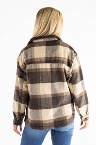 A woman viewed from the back wearing a brown, beige, and gray buffalo plaid flannel shirt jacket with blue jeans, set against a plain white background.